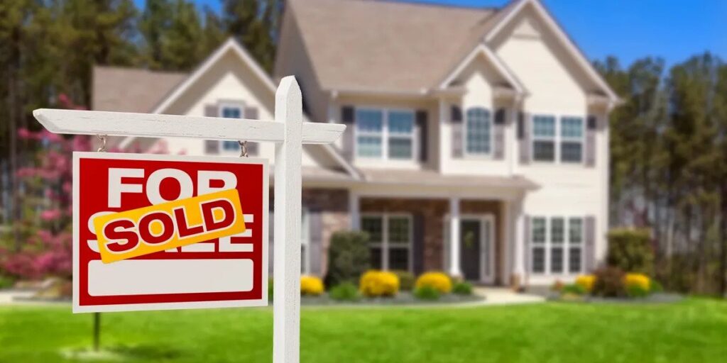 Live focus picture of a sold sign with a beautiful two-story suburban house in the background.